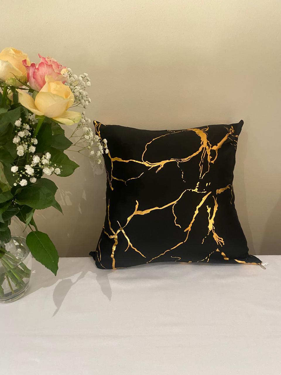 a black pillow with gold foil on it next to a vase of flowers